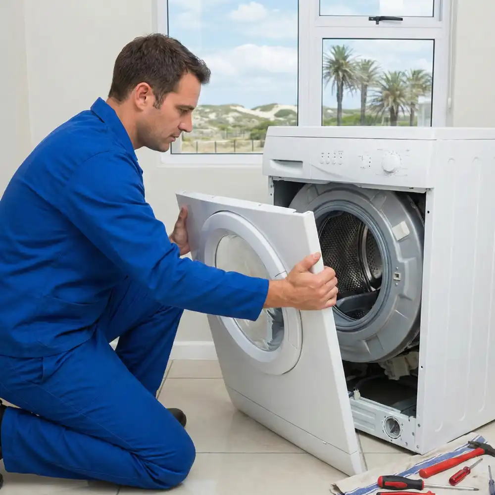 Appliance technician removing the front panel of a washing machine to check for sand clogs in a Wild Dunes home.